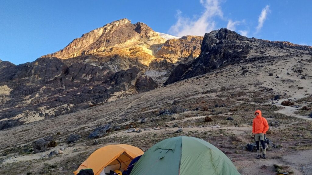Mountain tents at Arenales camp on Nevado del Tolima in Colombia, with climber and volcanic slopes at sunrise.