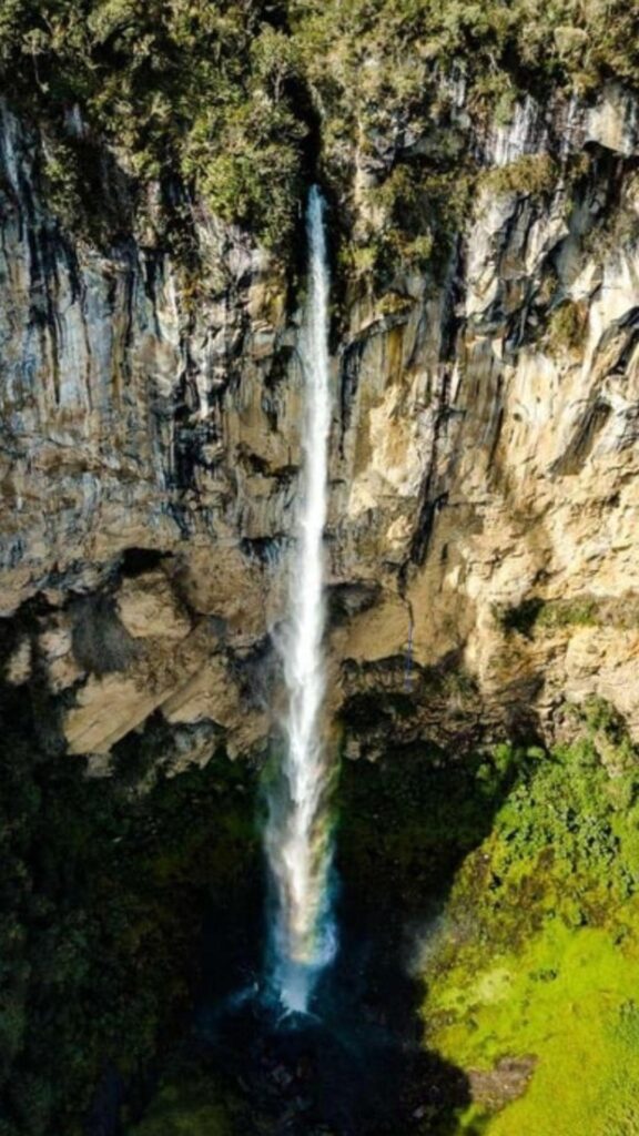 Cascada del Salto San Romualdo waterfall dropping from a high cliff into a pool surrounded by lush vegetation in Colombia.