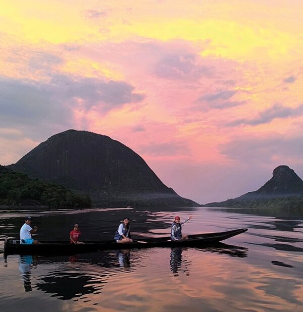 Travelers in traditional canoe at sunset in remote Colombia river landscape, sharing an experience with a local Indigenous community of mavecure, guainia