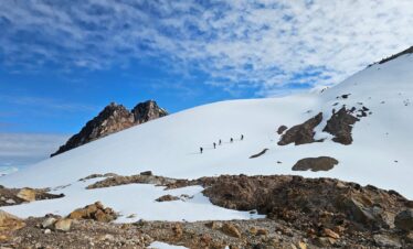Group of climbers traversing a wide snow slope on Nevado del Tolima in Colombia under a blue sky with scattered clouds.