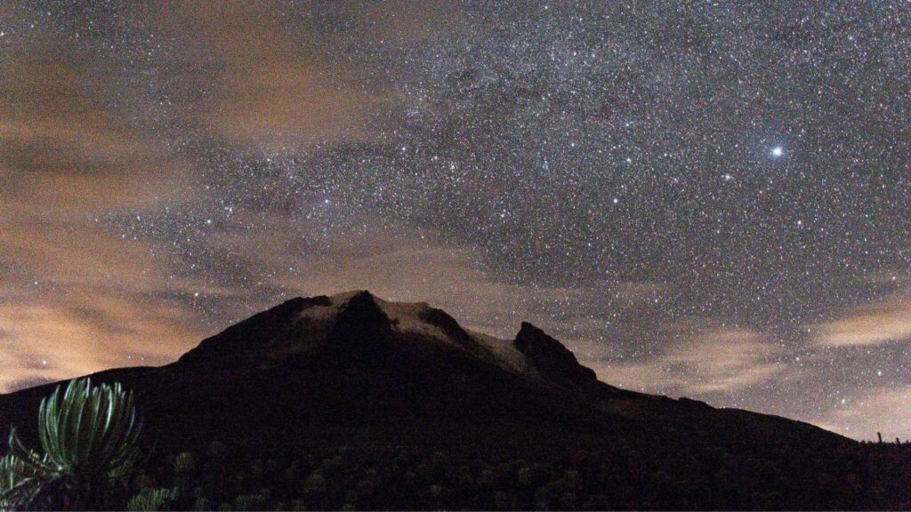 Star-filled night sky above Nevado del Tolima in Colombia, with the mountain silhouetted against the Milky Way.