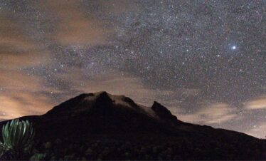 Star-filled night sky above Nevado del Tolima in Colombia, with the mountain silhouetted against the Milky Way.