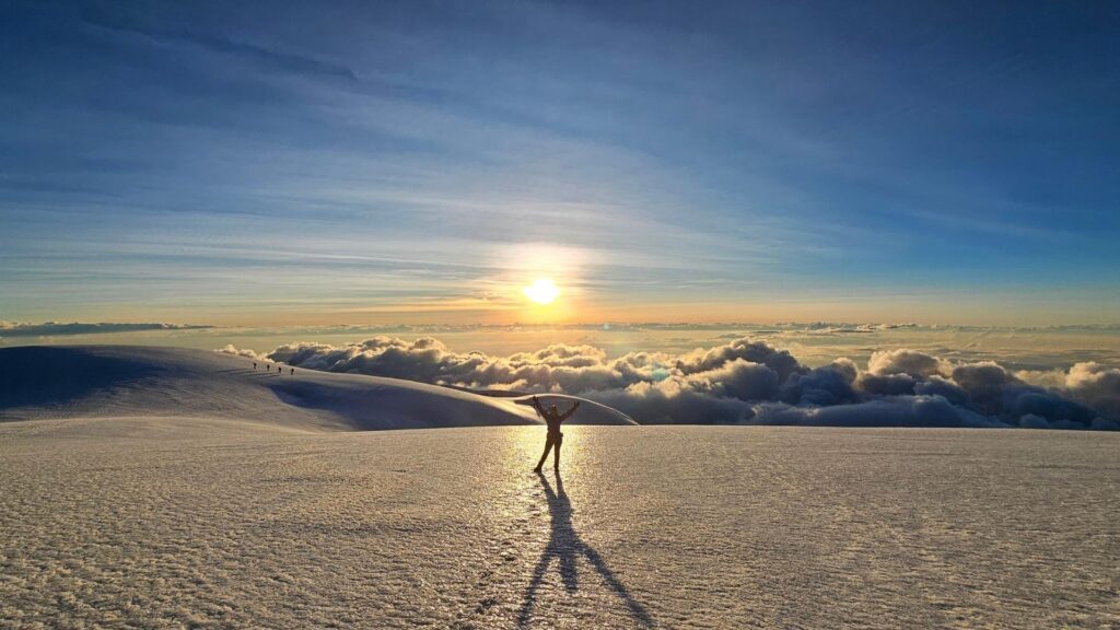 Silhouette of a climber celebrating on the summit of Nevado del Tolima in Colombia at sunrise above a sea of clouds.