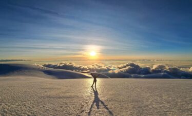 Silhouette of a climber celebrating on the summit of Nevado del Tolima in Colombia at sunrise above a sea of clouds.