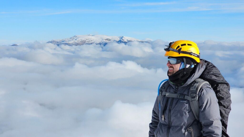 Climber standing above the clouds on Nevado del Tolima in Colombia, with Nevado del Ruiz visible in the background.