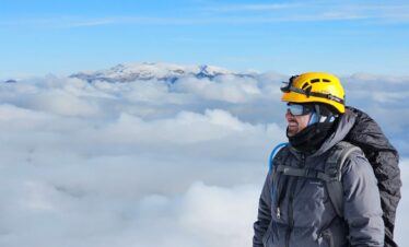 Climber standing above the clouds on Nevado del Tolima in Colombia, with Nevado del Ruiz visible in the background.