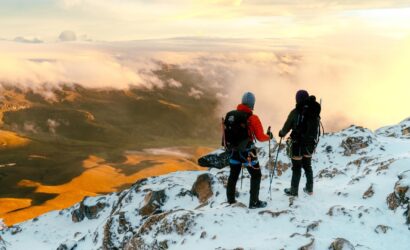 Two climbers standing on the snowy morane of Nevado del Tolima in Colombia, looking over clouds and a sunlit Andean valley at sunrise.