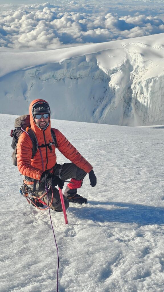 Mountaineer kneeling on glacier with ice axe near a crevasse on Nevado del Tolima.