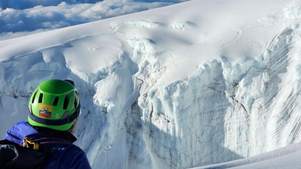 Mountaineer in helmet observing a large crevasse and glacier wall on Nevado del Tolima.