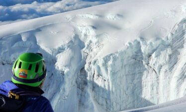 Mountaineer in helmet observing a large crevasse and glacier wall on Nevado del Tolima.