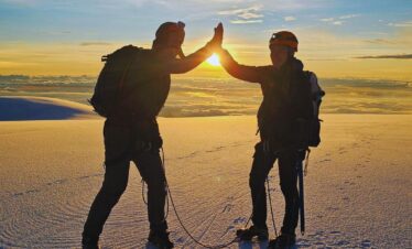 Two climbers high-fiving on the summit of Nevado del Tolima at sunrise above the clouds.