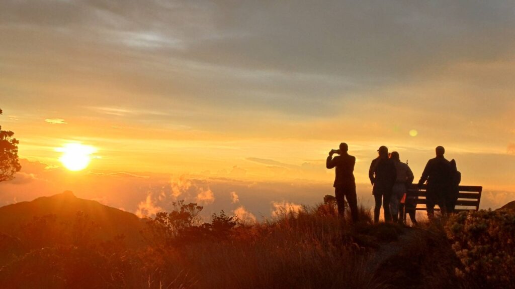 Visitors watching a colorful sunset from El Cisne viewpoint above the clouds in Los Nevados National Natural Park, Colombia.