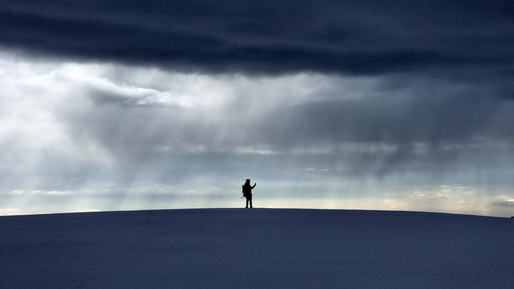 Solo trekker crossing the Santa Isabel Glacier beneath dramatic storm clouds in Los Nevados National Natural Park, Colombia.