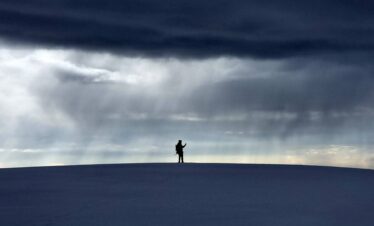 Solo trekker crossing the Santa Isabel Glacier beneath dramatic storm clouds in Los Nevados National Natural Park, Colombia.
