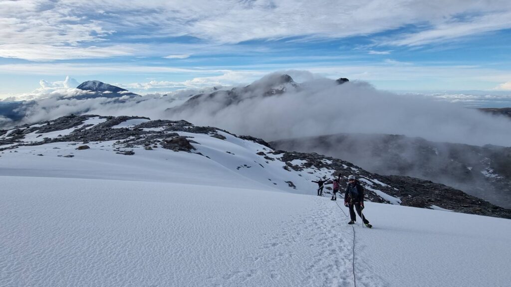 Mountaineers roped together crossing the Nevado Santa Isabel glacier above the clouds, with snow-covered volcanic peaks visible in Los Nevados National Natural Park, Colombia.