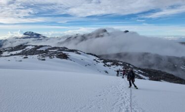 Mountaineers roped together crossing the Nevado Santa Isabel glacier above the clouds, with snow-covered volcanic peaks visible in Los Nevados National Natural Park, Colombia.