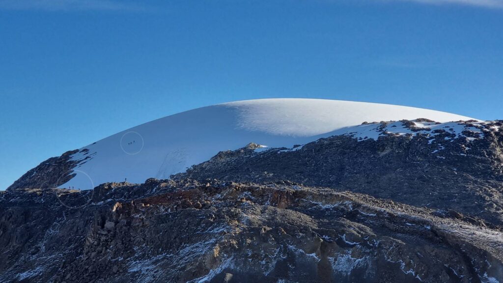 Tiny hikers crossing the vast Nevado Santa Isabel glacier, illustrating the immense scale of the tropical glacier against rugged volcanic terrain in Colombia.