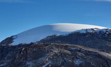 Tiny hikers crossing the vast Nevado Santa Isabel glacier, illustrating the immense scale of the tropical glacier against rugged volcanic terrain in Colombia.