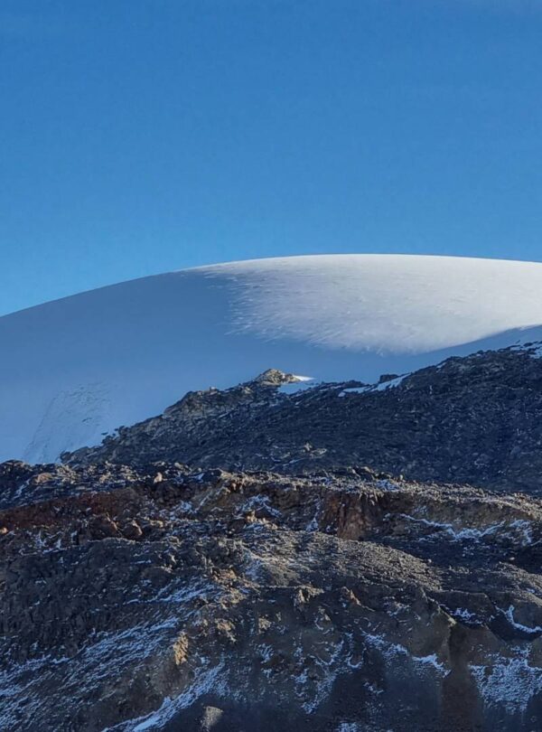 Tiny hikers crossing the vast Nevado Santa Isabel glacier, illustrating the immense scale of the tropical glacier against rugged volcanic terrain in Colombia.
