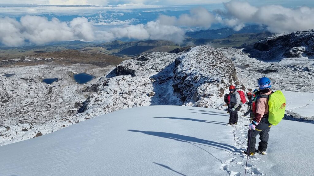 Roped mountaineers standing on the Nevado Santa Isabel glacier overlooking Laguna Verde and the high-altitude landscapes of Los Nevados National Natural Park, Colombia.