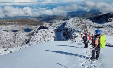 Roped mountaineers standing on the Nevado Santa Isabel glacier overlooking Laguna Verde and the high-altitude landscapes of Los Nevados National Natural Park, Colombia.