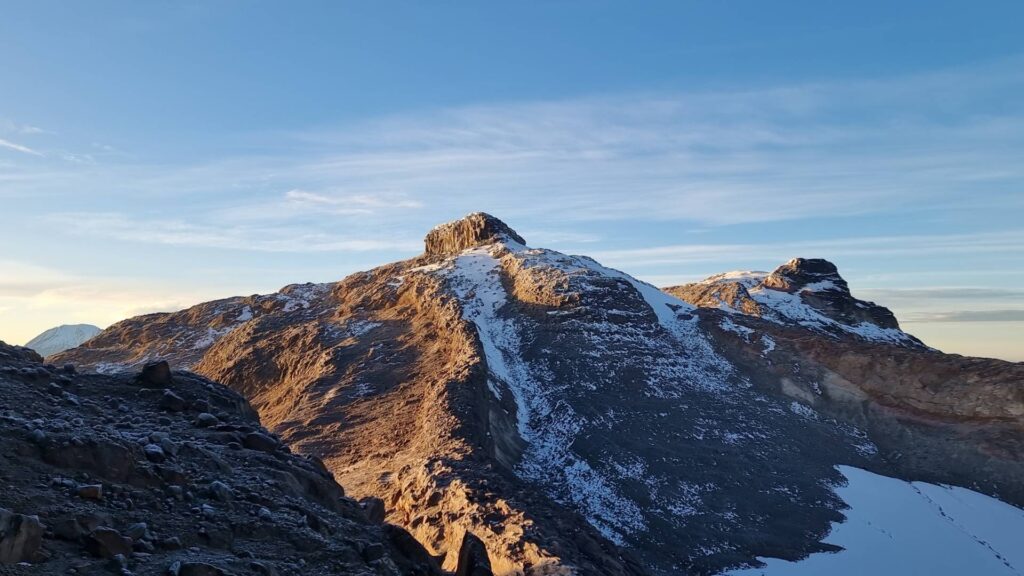 South and Central summits of Nevado Santa Isabel illuminated by sunrise light, with snow patches and volcanic terrain in Los Nevados National Natural Park, Colombia.