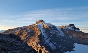 South and Central summits of Nevado Santa Isabel illuminated by sunrise light, with snow patches and volcanic terrain in Los Nevados National Natural Park, Colombia.