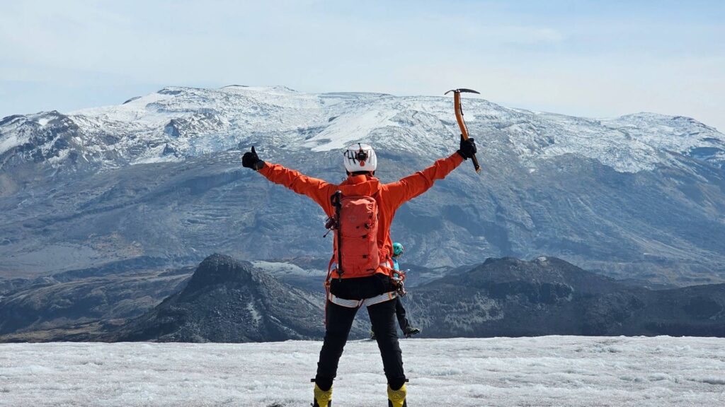 Mountaineer celebrating on Nevado Santa Isabel glacier with ice axe during a guided glacier hike in Los Nevados National Natural Park, Colombia