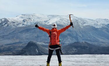 Mountaineer celebrating on Nevado Santa Isabel glacier with ice axe during a guided glacier hike in Los Nevados National Natural Park, Colombia