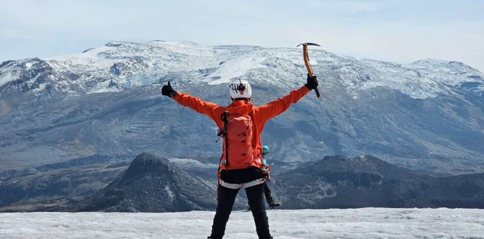 Mountaineer celebrating on Nevado Santa Isabel glacier with ice axe during a guided glacier hike in Los Nevados National Natural Park, Colombia