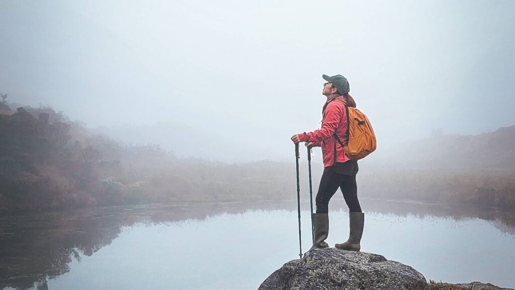 Hiker standing beside a misty high-altitude lagoon in the páramo ecosystem of the Colombian Andes.