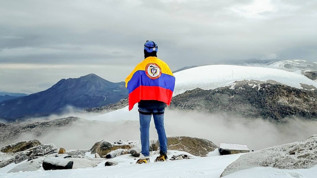 Mountaineer wrapped in the Colombian flag overlooking the Santa Isabel Glacier in Los Nevados National Natural Park, Colombia.