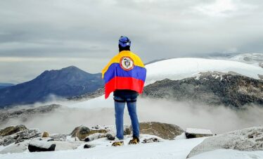 Mountaineer wrapped in the Colombian flag overlooking the Santa Isabel Glacier in Los Nevados National Natural Park, Colombia.